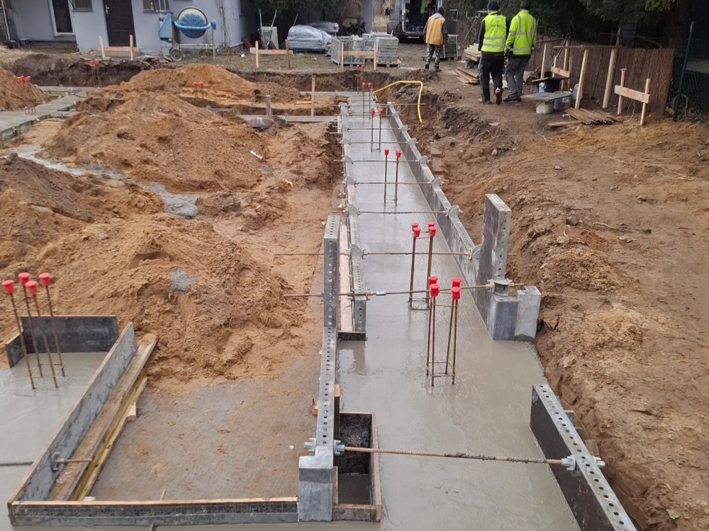 Wylewane ławy fundamentowe z widocznym zbrojeniem i deskowaniem na terenie budowy
