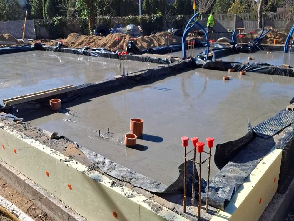 Płyta fundamentowa wylewana na budowie, z widocznym zbrojeniem i rurami instalacyjnymi