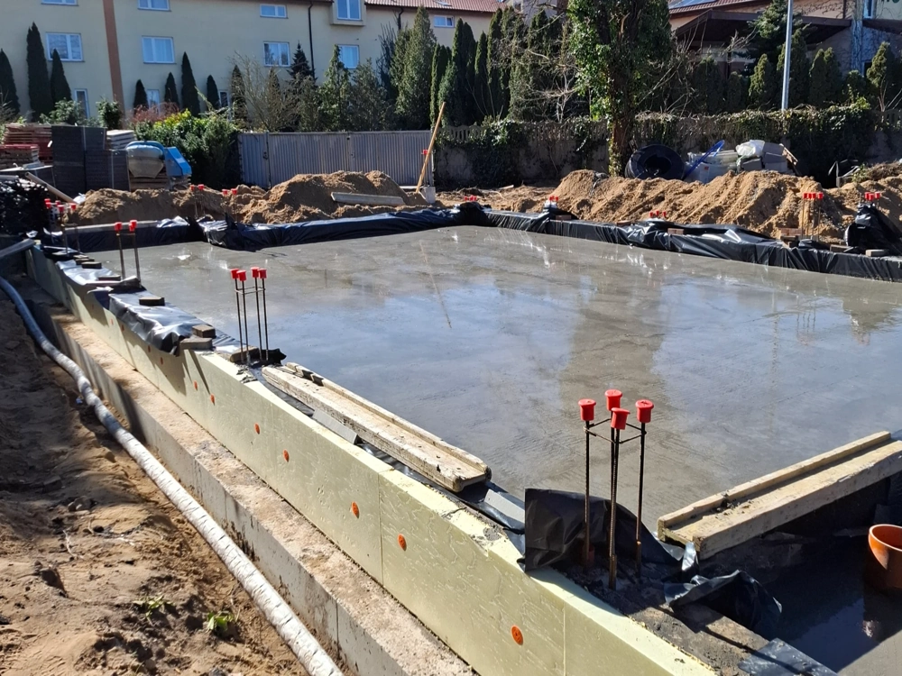 Wylewana płyta fundamentowa z izolacją termiczną i wystającym zbrojeniem na placu budowy