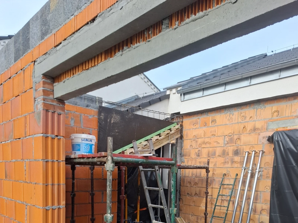 Stan surowy otwarty budynku z murowanymi ścianami z bloczków ceramicznych, zbrojeniem konstrukcji i rusztowaniem