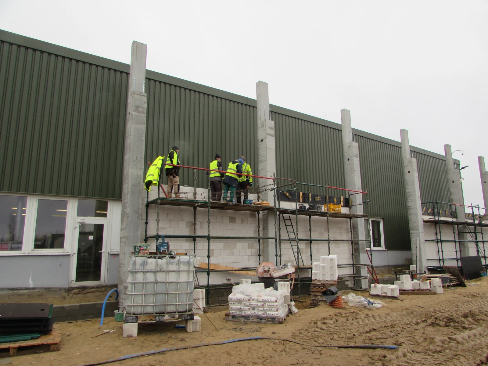 Pracownicy murowania ścian z bloczków na rusztowaniu pod elewacją budynku