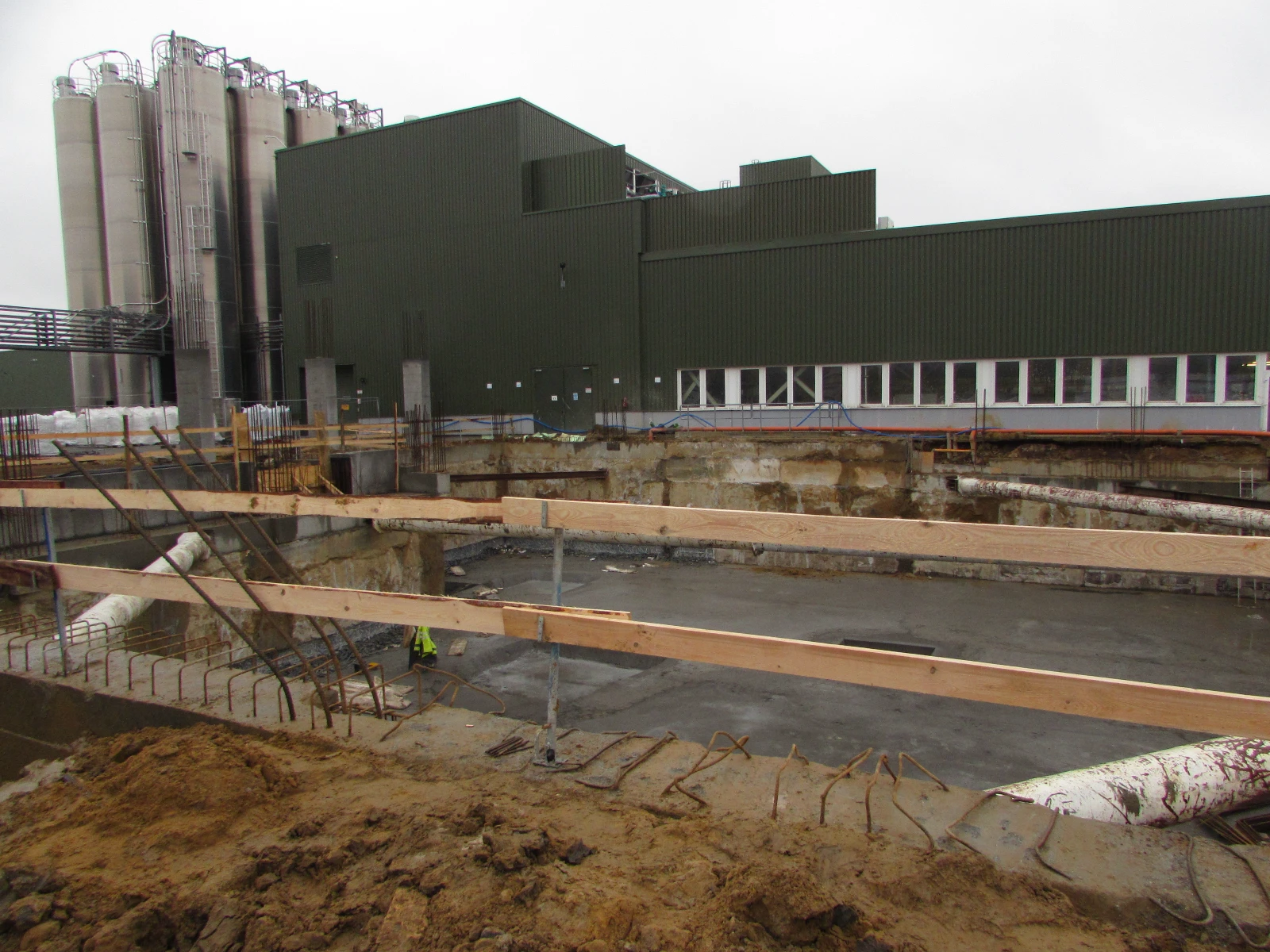 Plac budowy z wykopem i świeżo wylaną płytą fundamentową oraz zbrojeniem przy hali przemysłowej