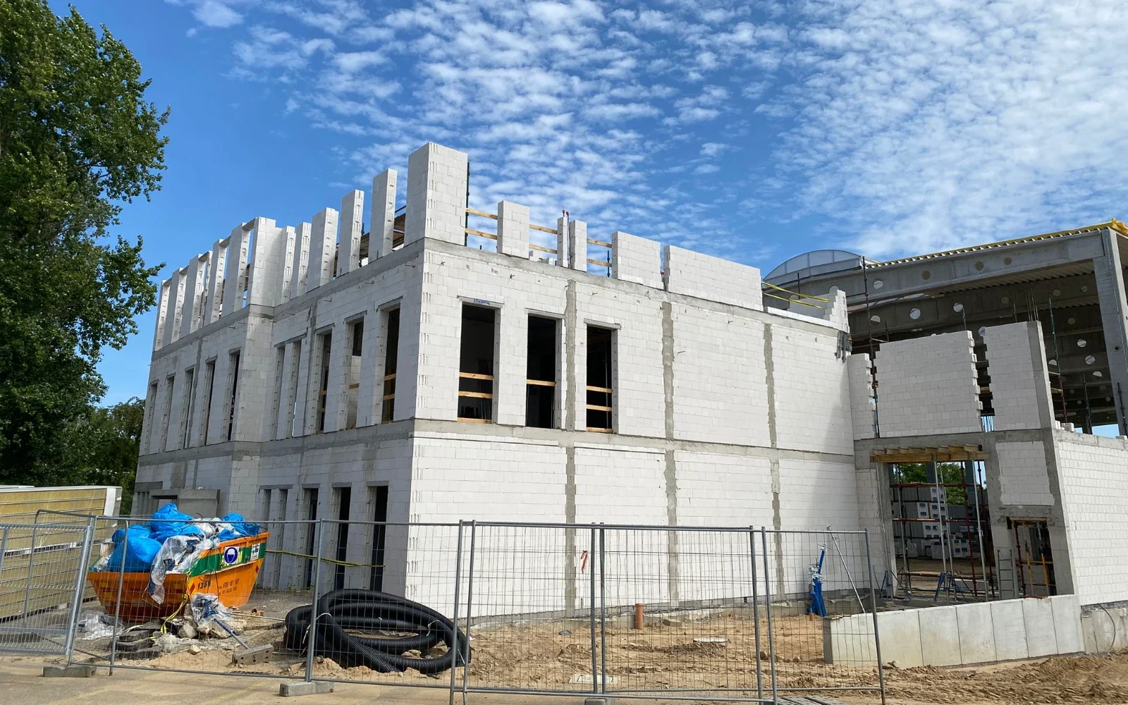 Stan surowy otwarty budynku z murowanymi ścianami z bloczków betonowych i ogrodzeniem placu budowy