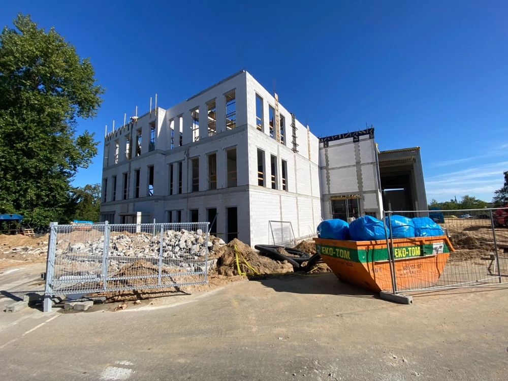 Stan surowy otwarty trzykondygnacyjnego budynku z pracami ziemnymi i fundamentami