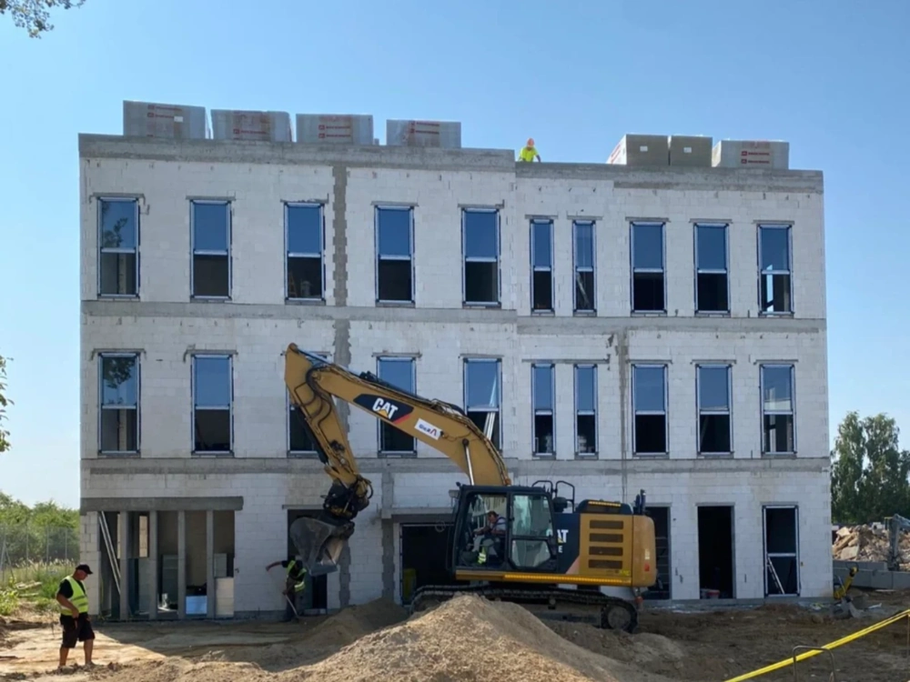 Koparka wykonująca Prace ziemne przy trzykondygnacyjnym szkielecie budynku z betonowych bloczków