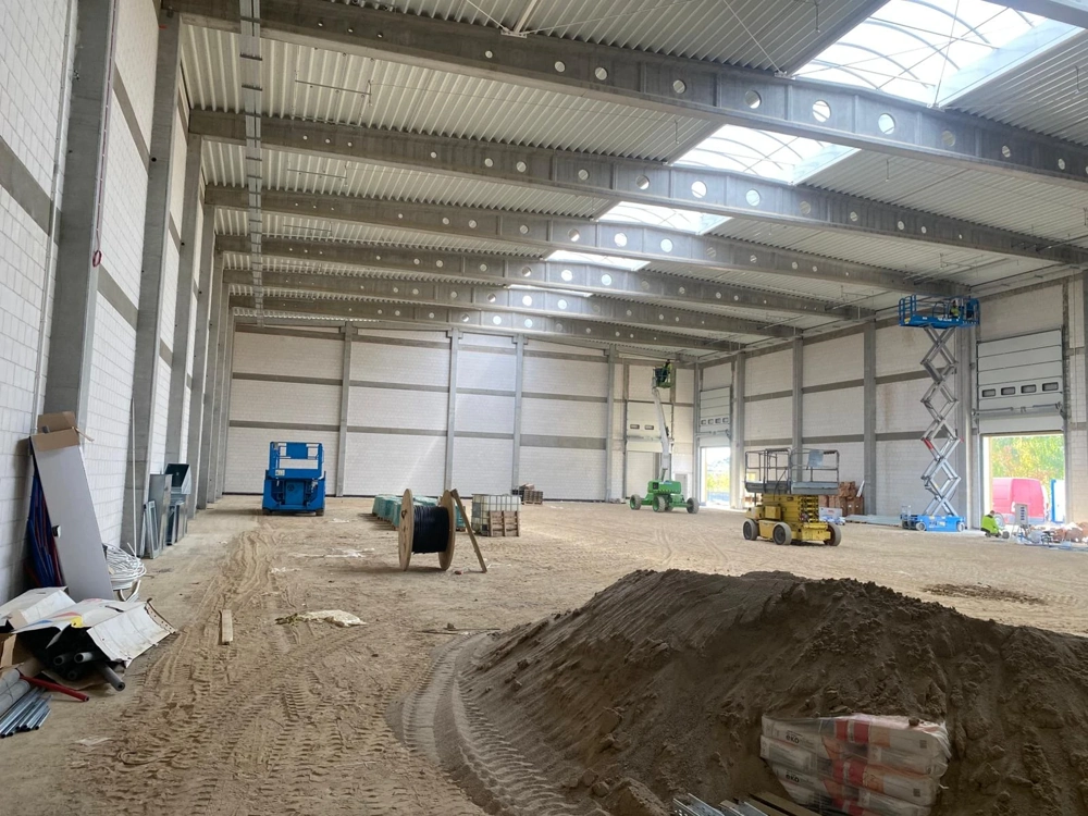 Wnętrze hali w stanie surowym otwartym z pracami ziemnymi i podnośnikami nożycowymi