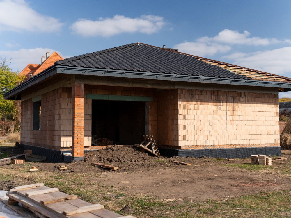 Dom jednorodzinny w stanie surowym otwartym z murowanymi ścianami, konstrukcją dachu i pracami ziemnymi
