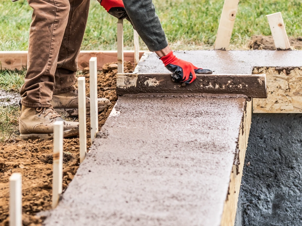 Pracownik wyrównuje powierzchnię świeżo wylanej płyty fundamentowej