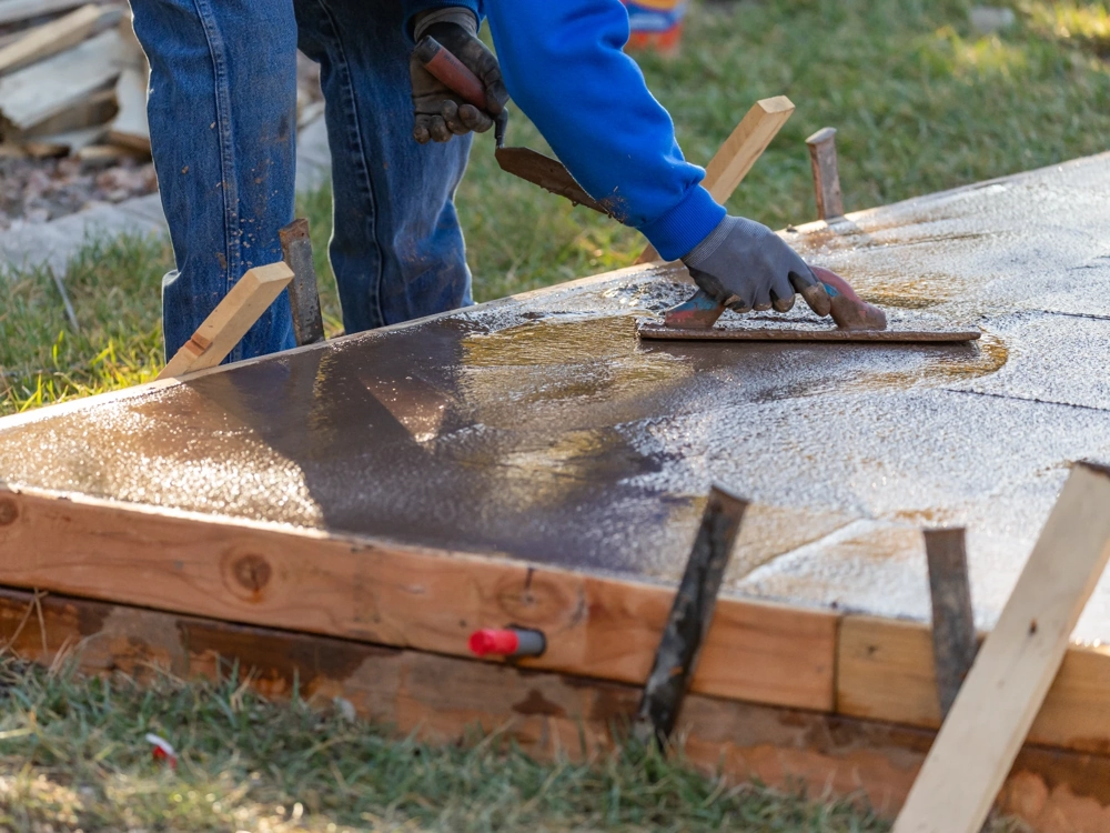 Robotnik wyrównuje świeżą płytę fundamentową w drewnianym szalunku