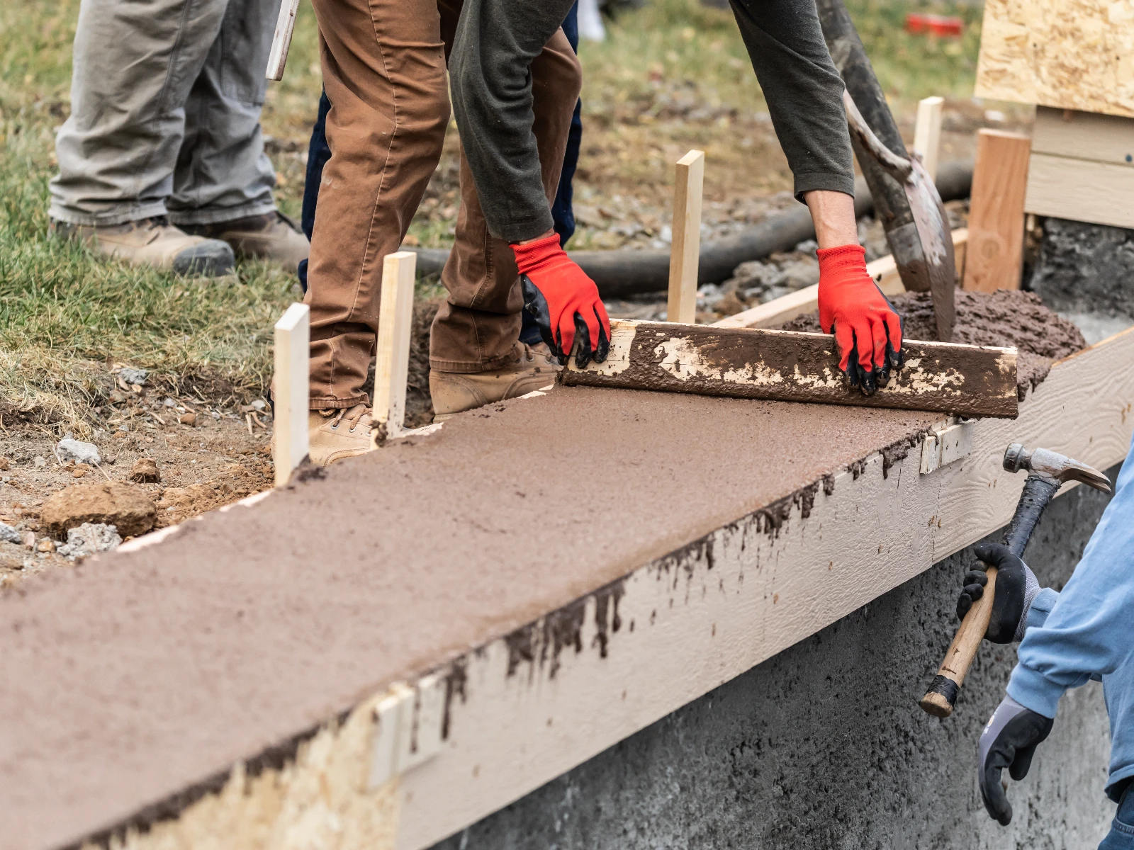 Pracownik wyrównuje świeżo wylaną ławę fundamentową przy użyciu łaty do betonu