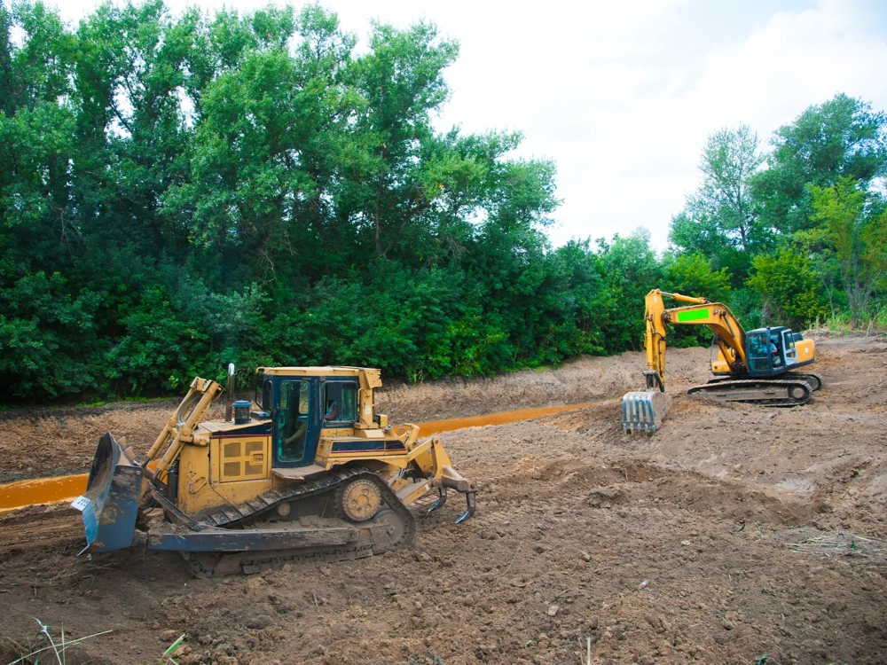 Koparka i spychacz wykonujące prace ziemne przy wykopie terenu